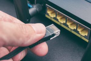 A close-up of a man's hand plugging an Ethernet cable into a router