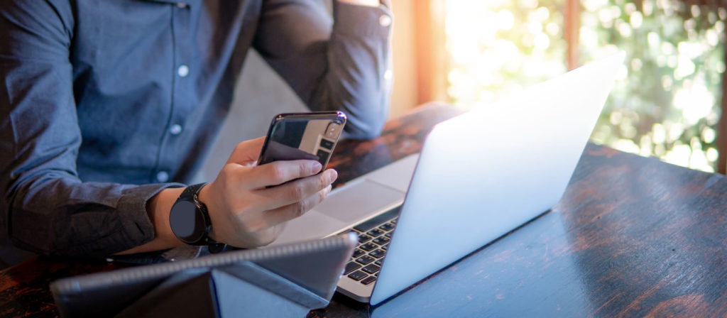 Man working on laptop using Cox internet holding smartphone