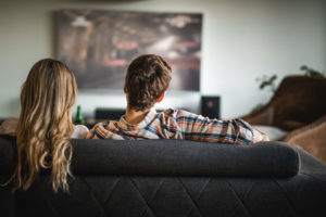 Para siedzi na kanapie w salonie oglądając telewizję kablową na dużym ekranie