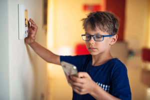 A young boy using a home security system and looking at a smart phone.