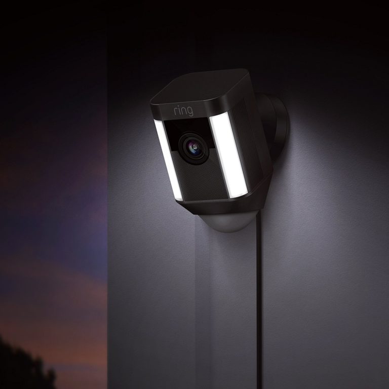 Ring spotlight camera shown mounted on a wall at nighttime with its spotlight turned on