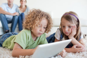 Serious children using a tablet computer while their happy parents are watching
