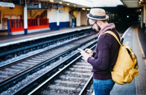 hipster man standing at train tracks looking at phone