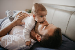 A man is laying down on a couch and kissing the baby he is holding to his chest.