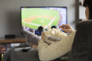Woman watching baseball on couch while eating popcorn