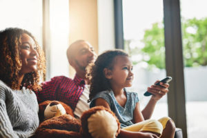 An African-American mom, dad, and daughter watch TV together on the couch