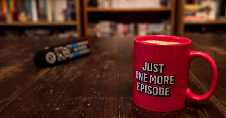 Photo of TV remote and coffee mug that is humourously labelled with "Just One More Episode"