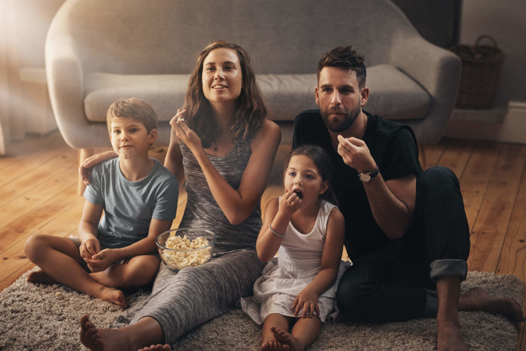 Family of four sitting on living room floor eating popcorn watching Hulu