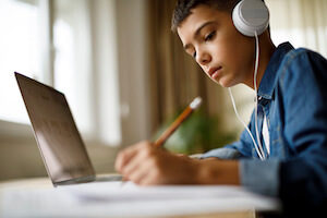 A teenage boy listens to music while doing homework on his laptop