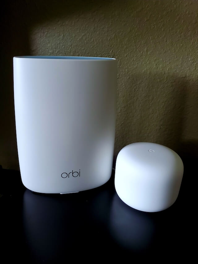 The small Nest Wi-Fi router sits next to a large Netgear Orbi router