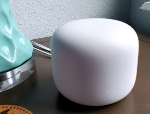 The Nest Wi-Fi router sits on a desk with a blue lamp