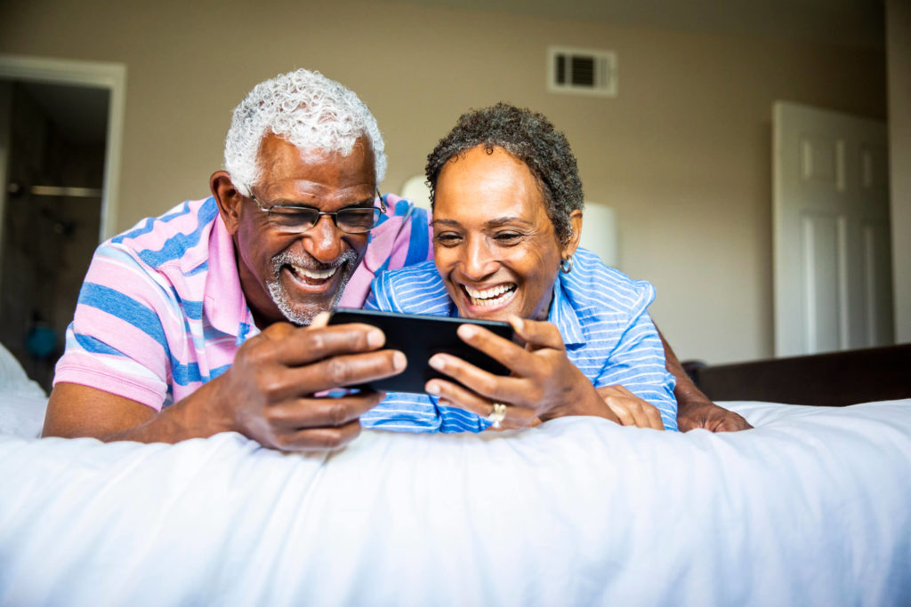 Couple laying on bed watching HBO Max on smartphone