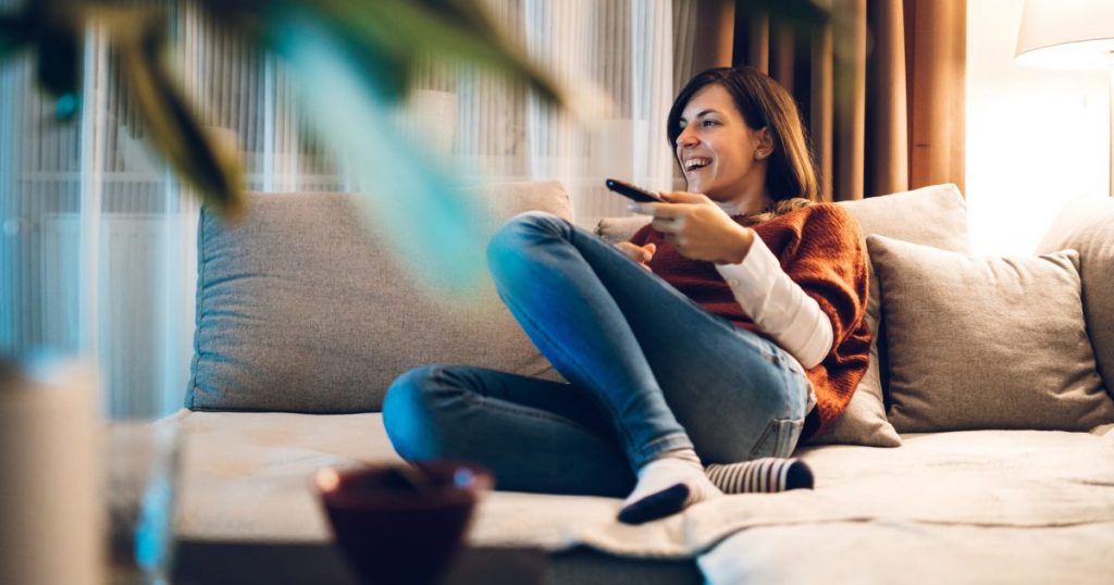 Woman laughing while watching TV relaxing on living room couch