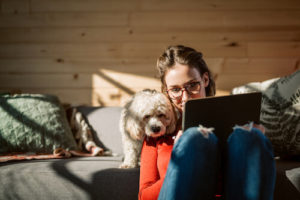 A woman sits with her dog and uses a tablet