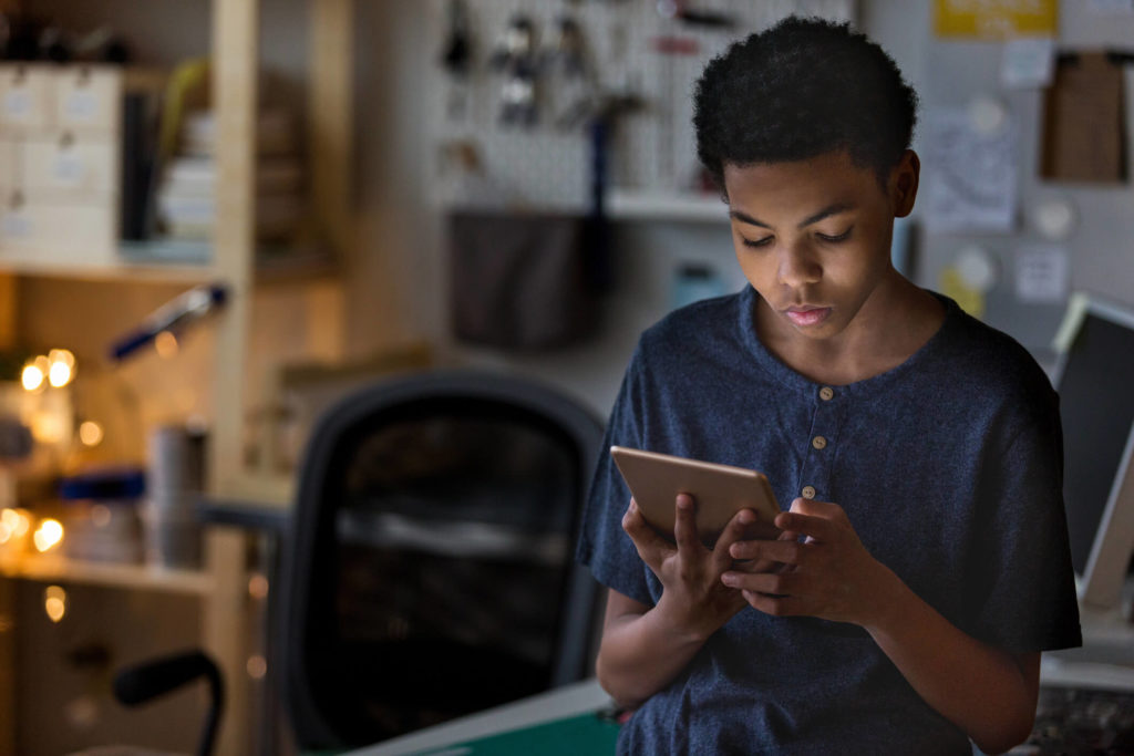 Teen boy streaming TV shows and movies on tablet in bedroom