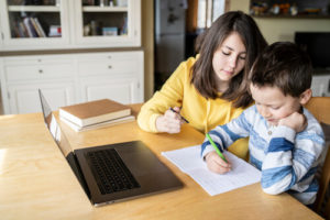 A sister helps her brother with homework on the computer