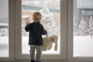 Small child standing at glass door looking out on a snowy yard
