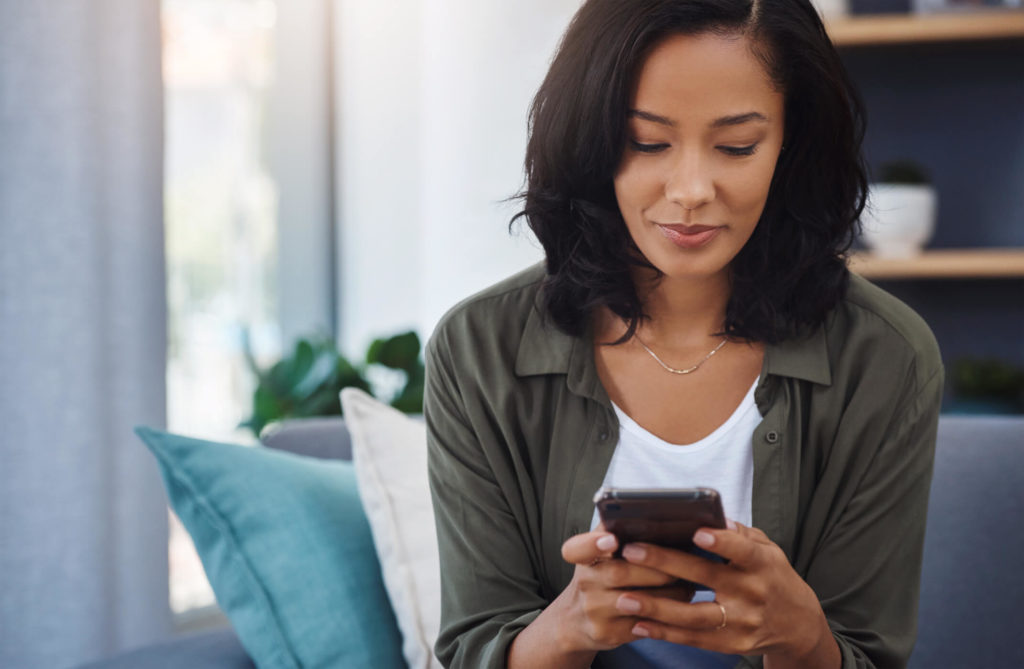 A woman sits on her couch looking at her mobile phone.