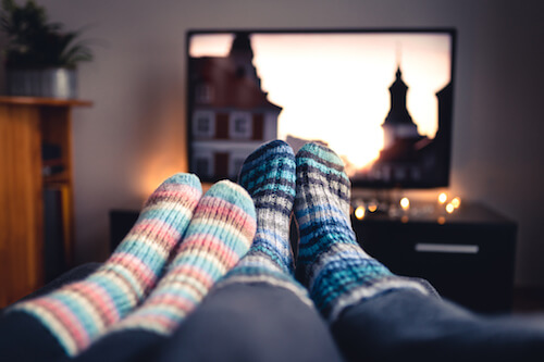A couple's feet wearing cozy socks in front of a TV screen streaming a movie