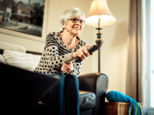 Grandmother sitting on couch in living room watching cable TV