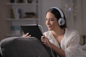 Woman watching streaming service on tablet with headphones on while sitting on couch