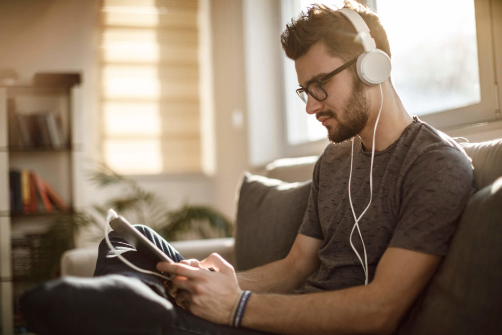 Young man watching streaming service on tablet with headphones sitting on couch