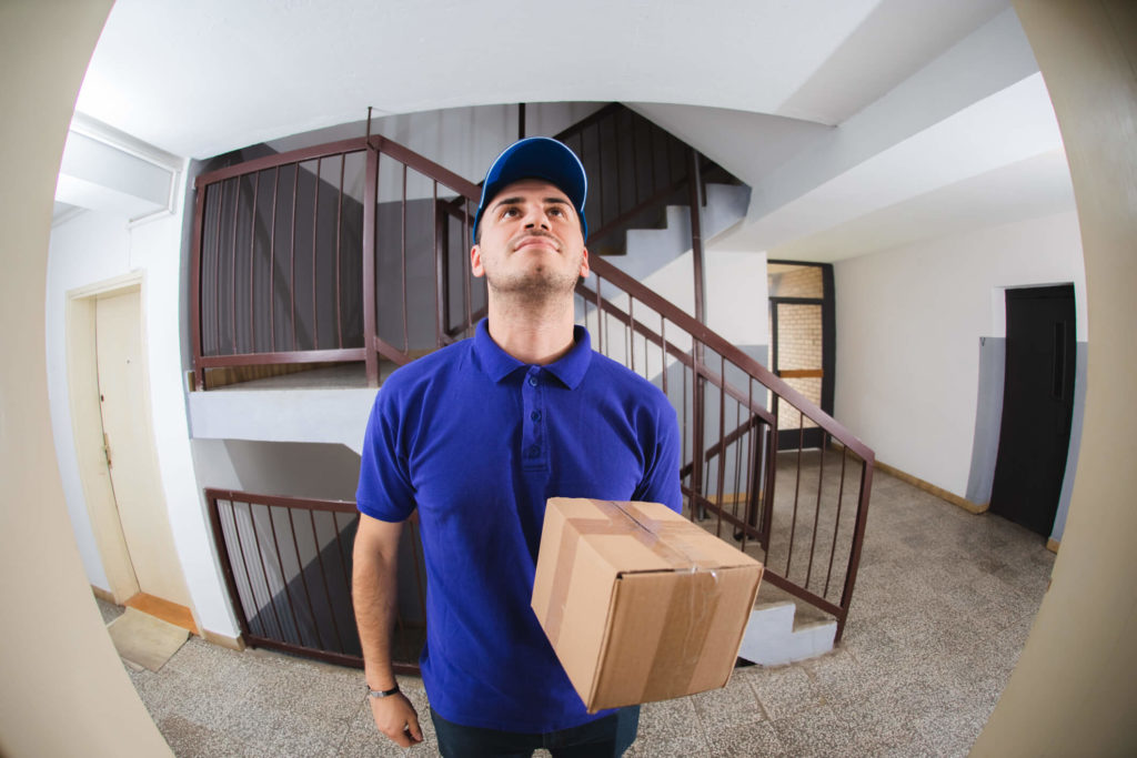 Man in a blue shirt seen through peephole standing holding package