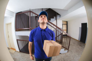 Man in a blue shirt seen through peephole standing holding package