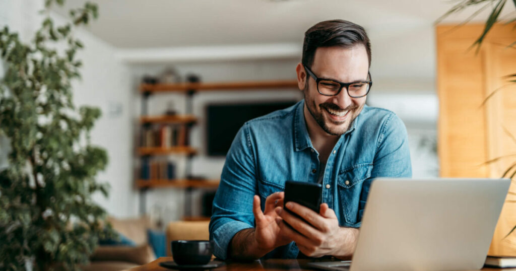 Photo of a man using his smartphone while using a VPN on his computer