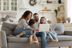 A mom, dad, and two children sit on a couch and use a laptop together
