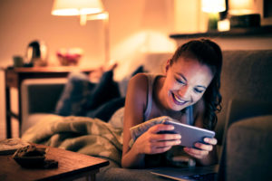 Young woman laying on living room couch on stomach while watching streaming service on smartphone
