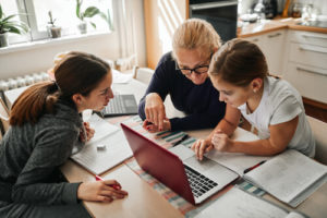 A mother helps her two daughters do homework on a laptop