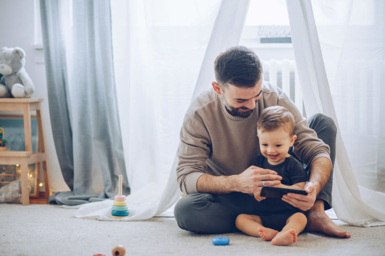 Father and young son sit on the floor together looking at a smartphone