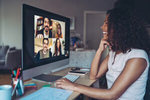A woman sits at her desk and videoconferences with four teammates