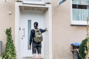 Person with baseball cap and backpack rings a doorbell