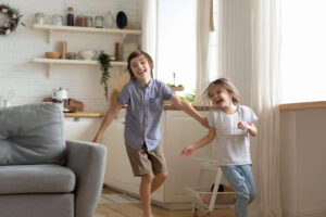 Two children smiling while running through a living room