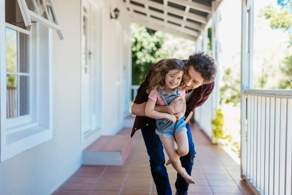 Father playing with young daughter on large porch of house