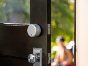 August Wi-Fi Smart Lock on a front door that is partially open showing a blurred person in the background