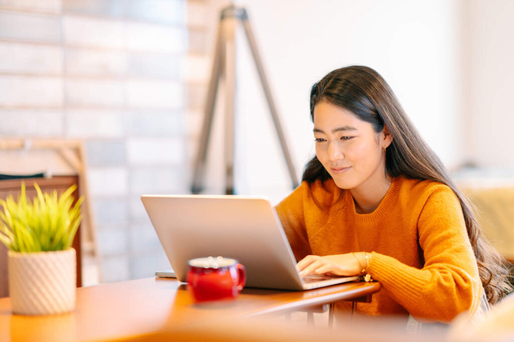 woman uses a computer at a table with a mug