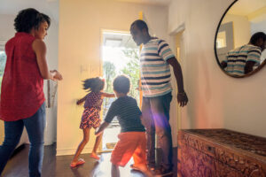 father holds open the door of a house as his family moves to go out the door