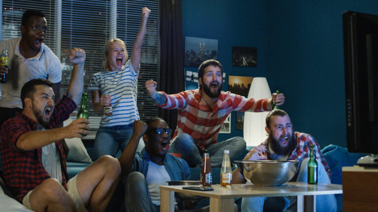 Group of friends cheering on sports team in living room