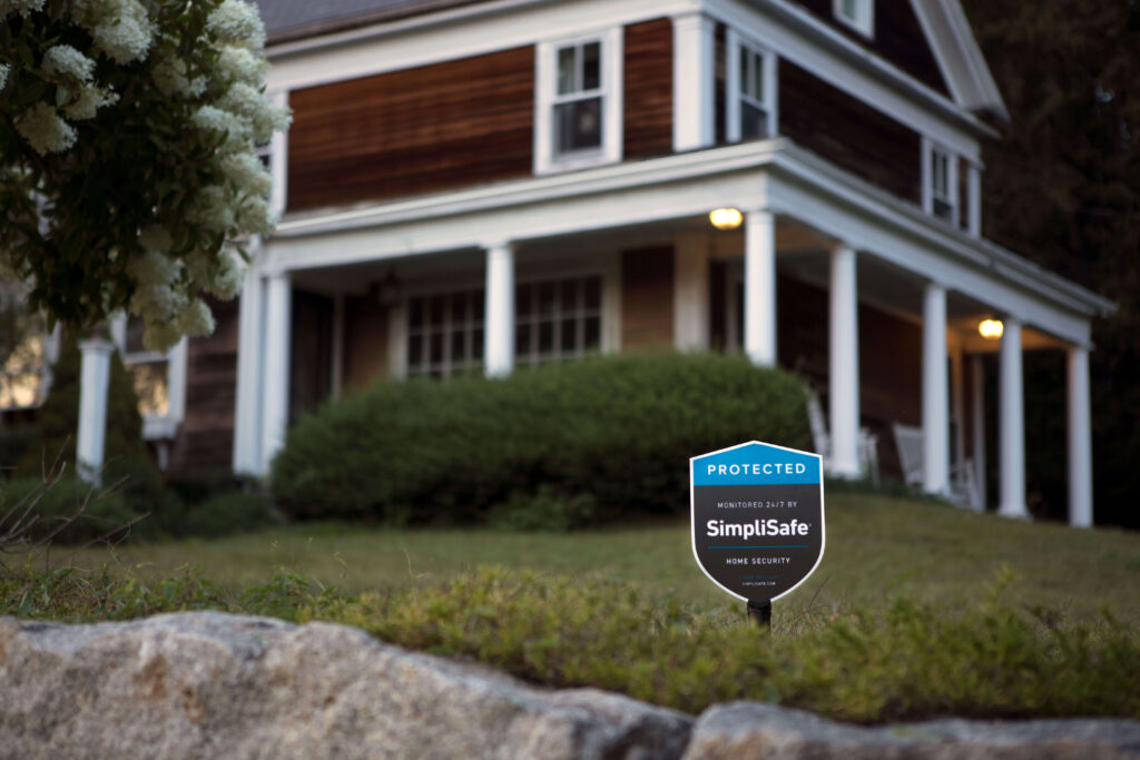 SimpliSafe yard sign in the lawn of a dark wood and white-colored house