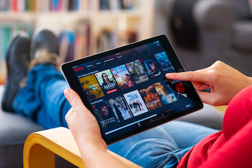 A man sits in a chair and surfs through Netflix on his tablet