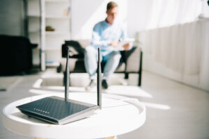 An internet router sits on a table in a living room with a man in a chair in the background