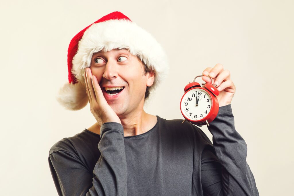 Photograph of a surprised man in a Santa hat holding a clock