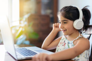 A young girl wears headphones and looks at her laptop