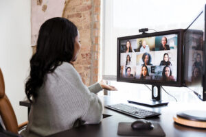 A woman sits at a desk and talks to her coworkers through video chat