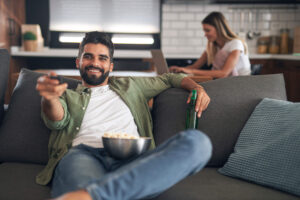 Man watching cable TV while eating popcorn and drinking a beer on the living room couch