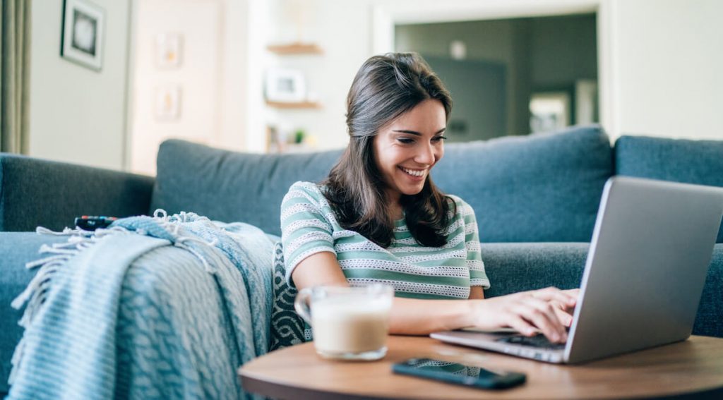 A woman sits on her couch and uses her laptop