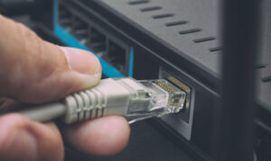 A close up of a hand plugging an Ethernet cable into a wireless router